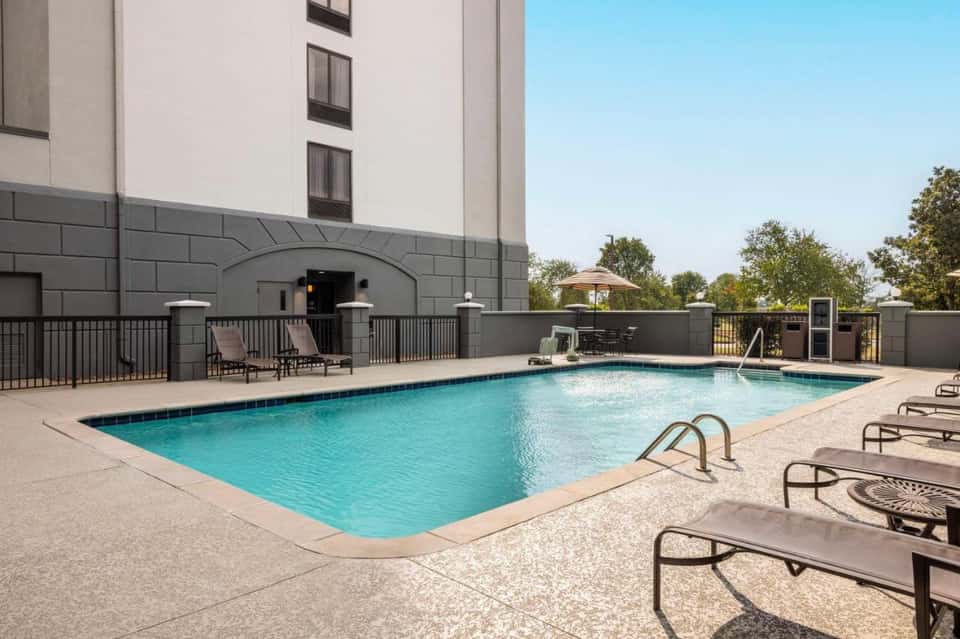 Modern hotel pool with rectangular shape, lounge chairs, building entrance with arched doorway, and clear sky