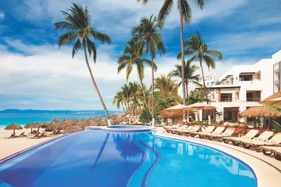 Beachfront resort pool with palm trees, lounge chairs, and oceanview overlooking tropical coastline