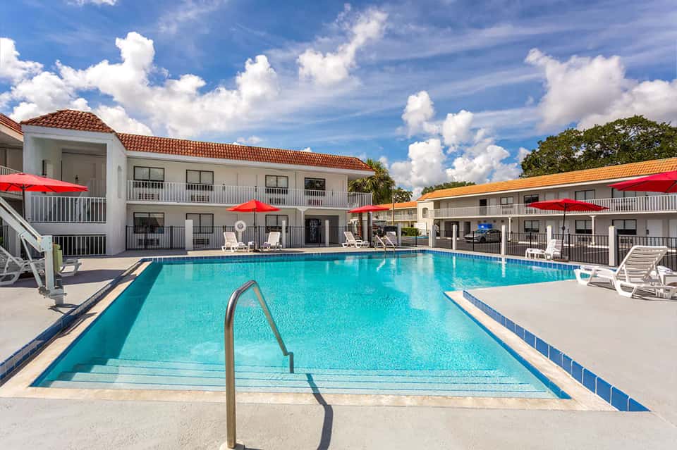 Rectangular swimming pool with metal railings, red umbrellas, and white hotel buildings in background