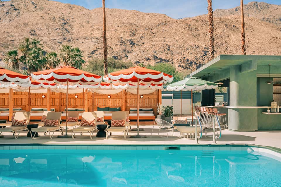 Vintage pool with red and white striped umbrellas, loungers, and mid-century modern poolside cabana