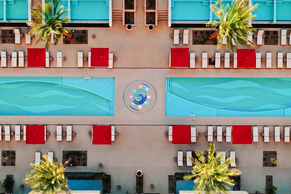 Aerial view of resort pools with bright turquoise water, red lounge chairs, and palm trees