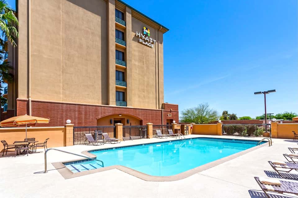 Hotel exterior with pool, lounge chairs, and yellow umbrellas under clear sky