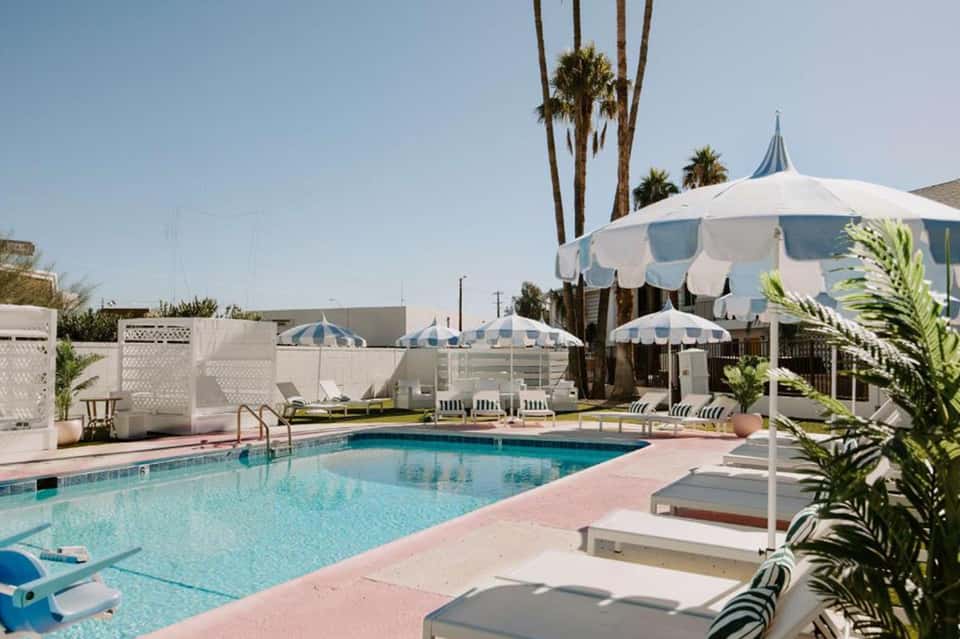 Vintage-style pool area with blue and white striped umbrellas, palm trees, and pink deck