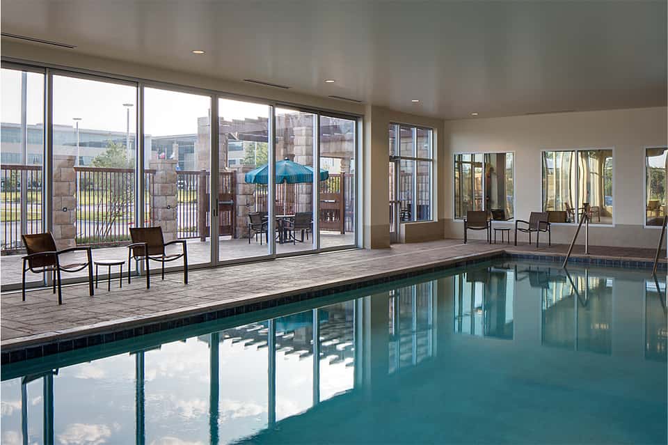Indoor hotel pool with floor-to-ceiling windows overlooking a city and outdoor terrace