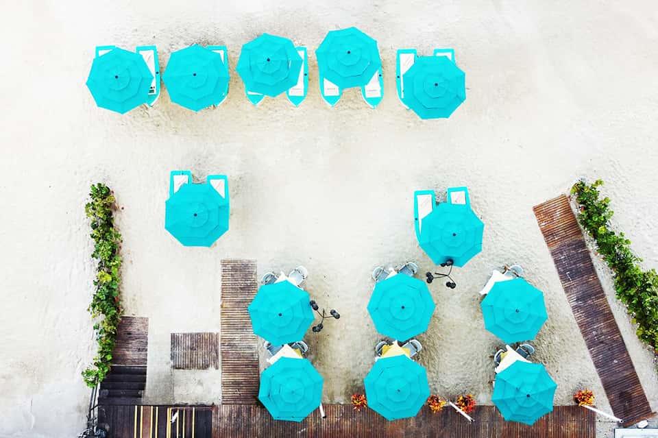 Aerial view of white sand beach with bright turquoise umbrellas and lounge chairs arranged in rows