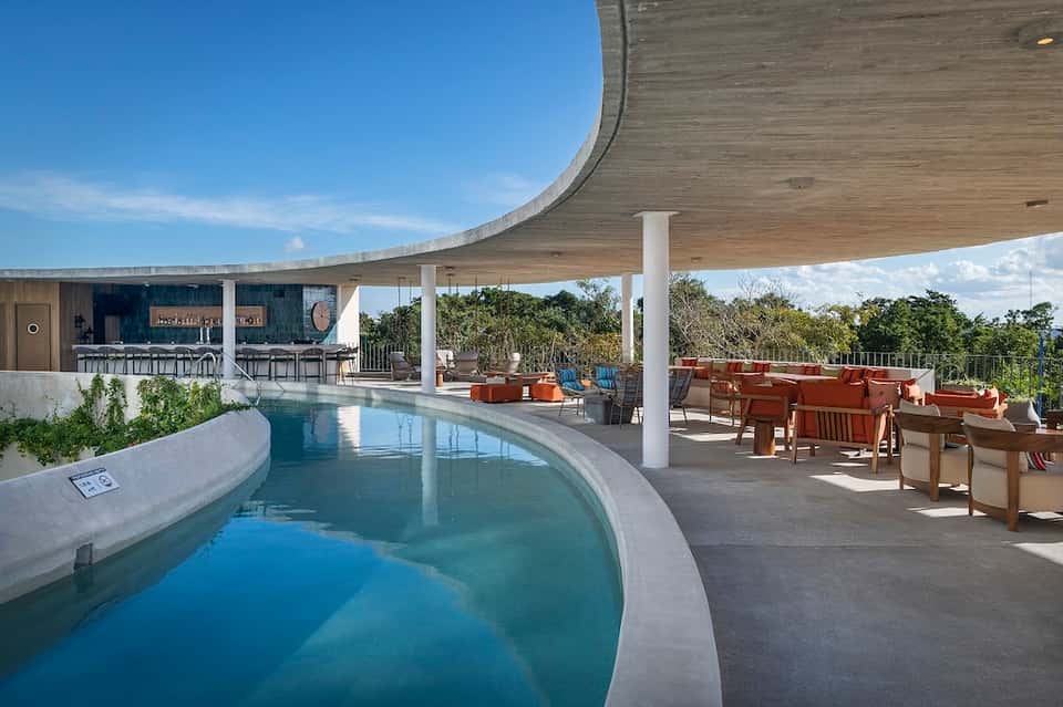 Modern curved architecture pool area with bar, lounge seating, and expansive terrace under curved canopy