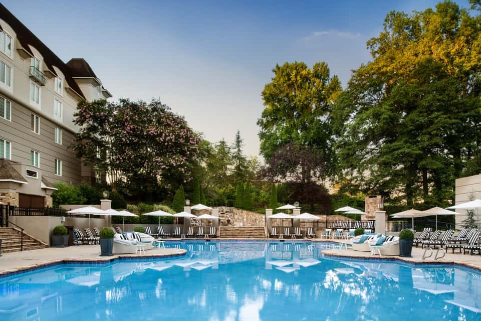 Elegant resort pool surrounded by white umbrellas, lounge chairs, and mature shade trees