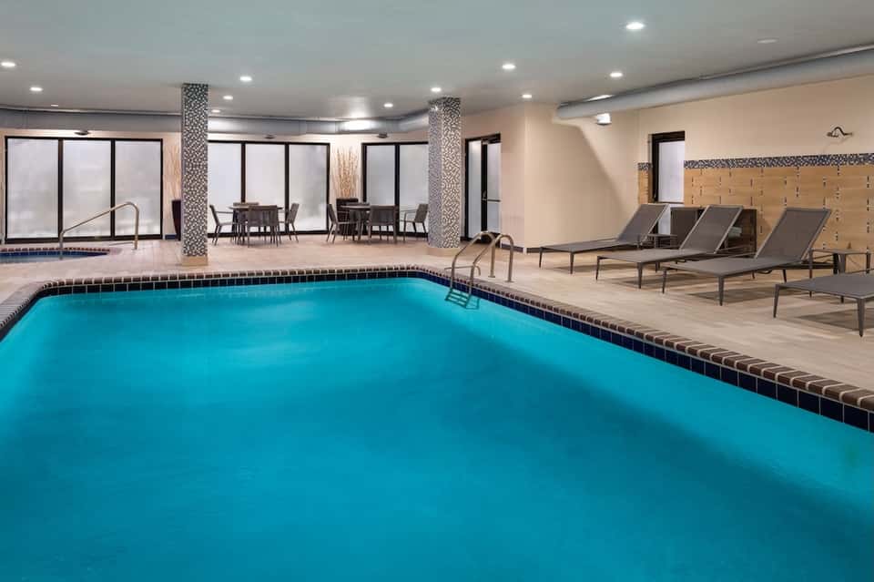Indoor pool with lap lanes, lounge chairs, columns, and windows overlooking outdoor areas