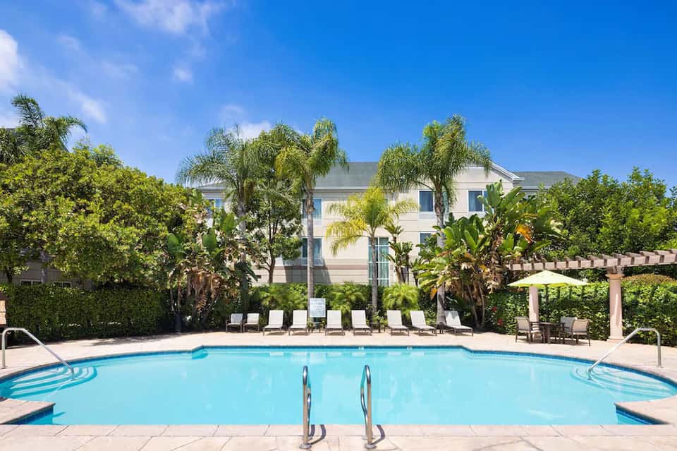 Resort pool surrounded by palm trees and lounge chairs with white umbrella on sunny day