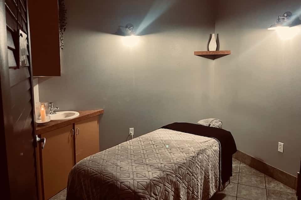 Spa treatment room with wooden vanity, white walls, and comfortable massage bed