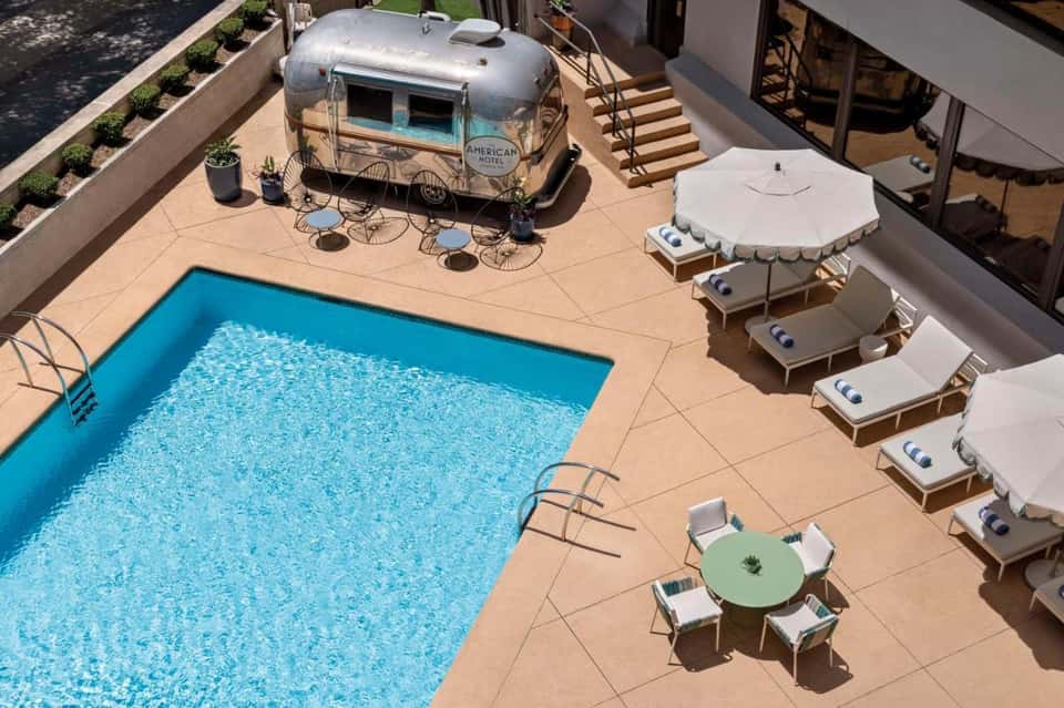 Courtyard pool with vintage Airstream trailer, lounge chairs, umbrella, and surrounding architecture