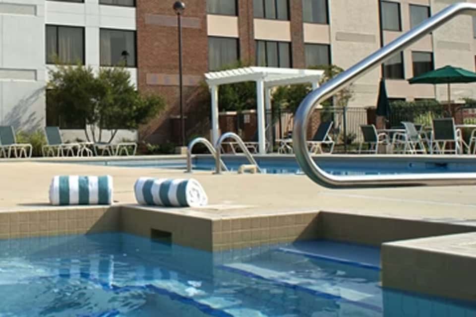 Indoor pool area with diving board, lounge chairs, and modern hotel building facade