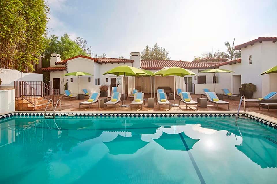 Resort pool with turquoise water, lounge chairs under lime green umbrellas, and Spanish architecture