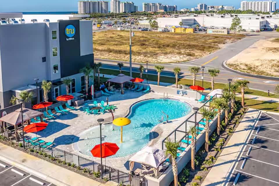 Colorful resort pool area with red umbrellas, turquoise water, and ocean city skyline