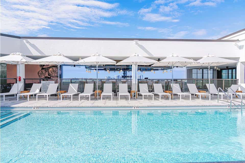 Rooftop pool with white lounge chairs, umbrellas, and city skyline views