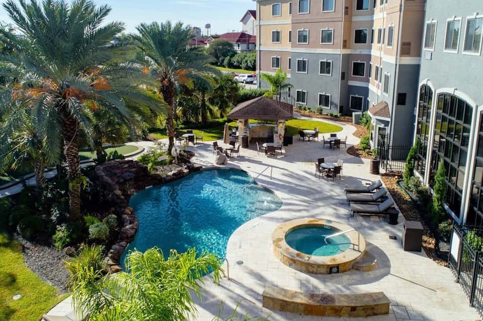 Aerial view of resort courtyard with curved pool, hot tub, palm trees, and lounge seating
