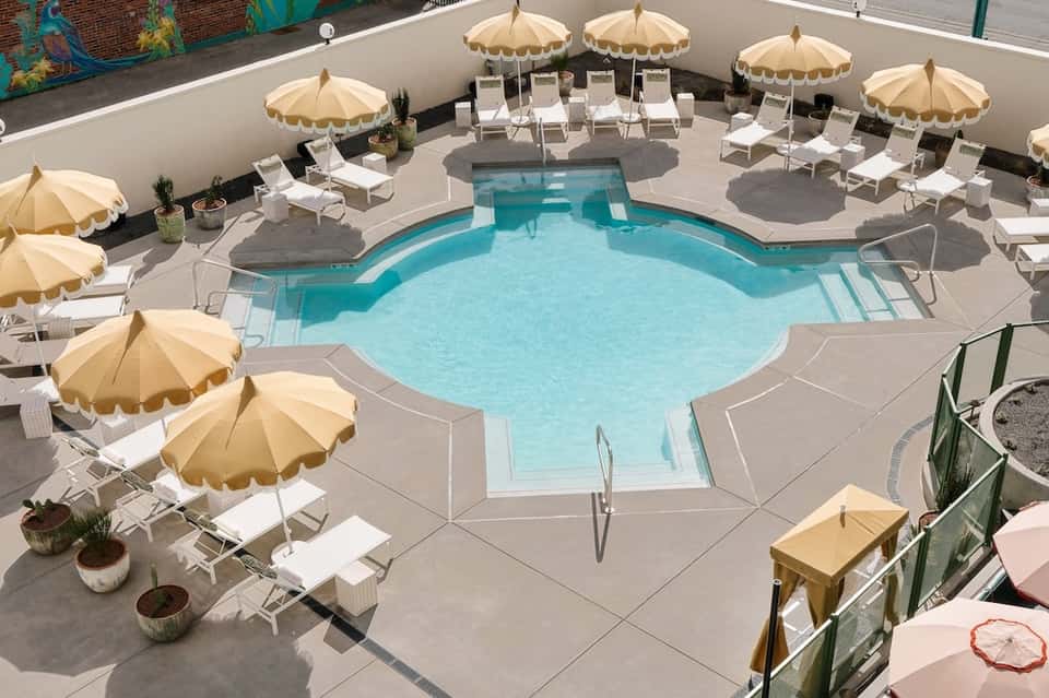 Curved turquoise pool surrounded by cream umbrellas, white lounge chairs, and white perimeter walls