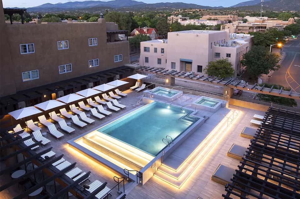 Rooftop pool area at dusk with lounge chairs, glowing lights, and mountain city views