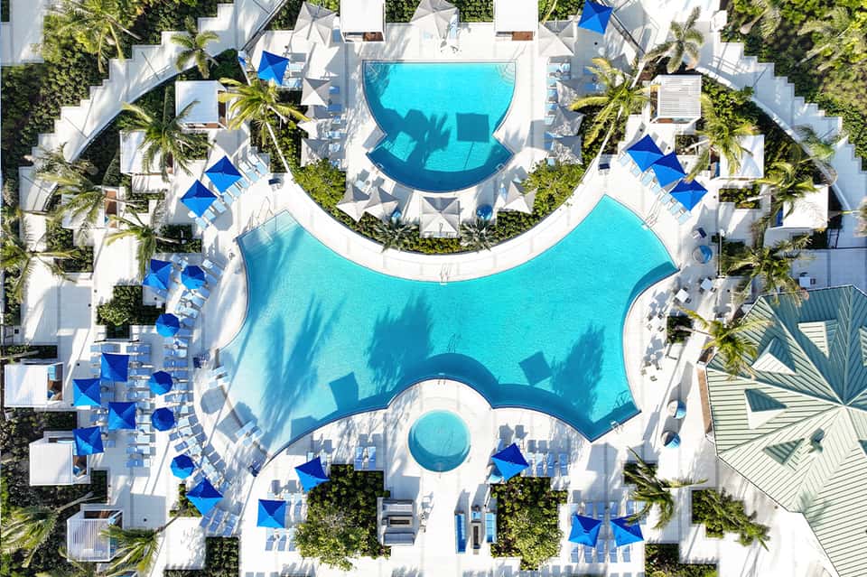 Aerial view of resort pools and white umbrellas surrounded by palm trees