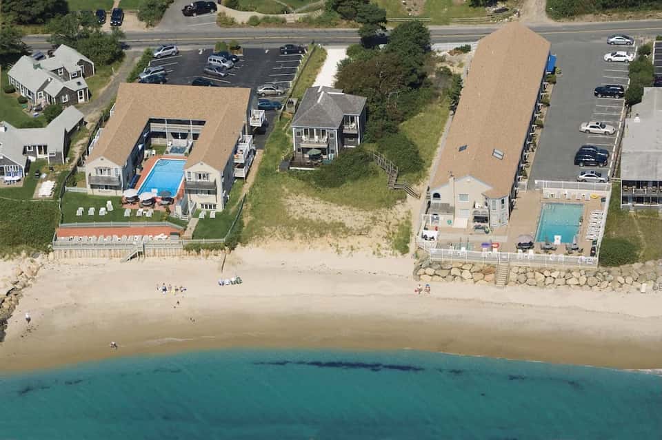 Aerial view of beachfront resort with pools, cottages, parking, and sandy beach