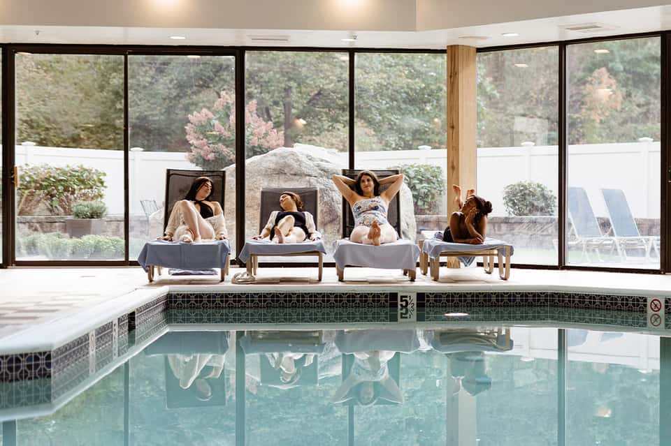 Indoor heated pool with large windows, guests relaxing on loungers overlooking landscape