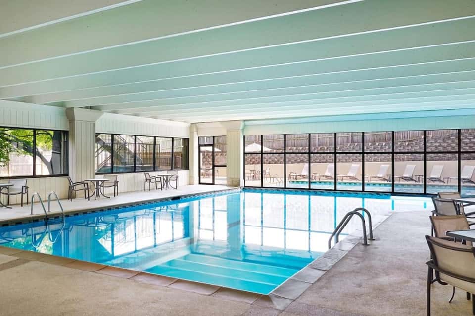 Indoor heated swimming pool with large windows overlooking outdoor pool deck