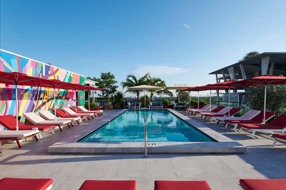 Resort pool with colorful umbrellas, red lounge chairs, and palm trees