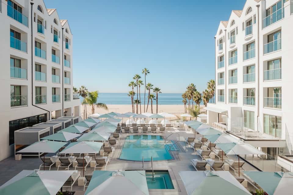 Beachfront resort pool area with turquoise umbrellas, loungers, and ocean view between buildings