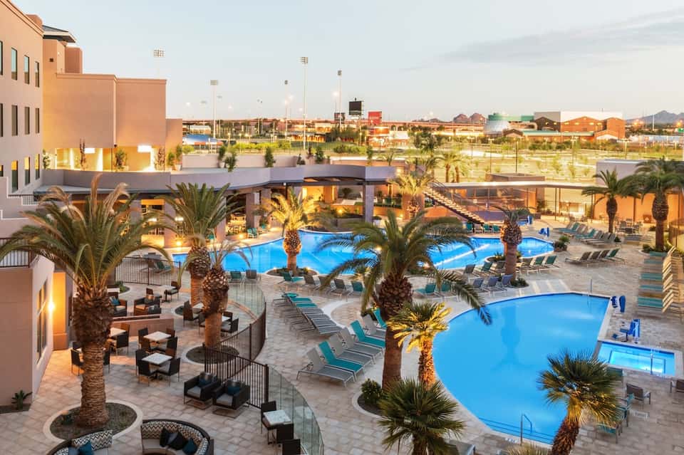 Aerial view of large resort complex with multiple pools, palm trees, and loungers