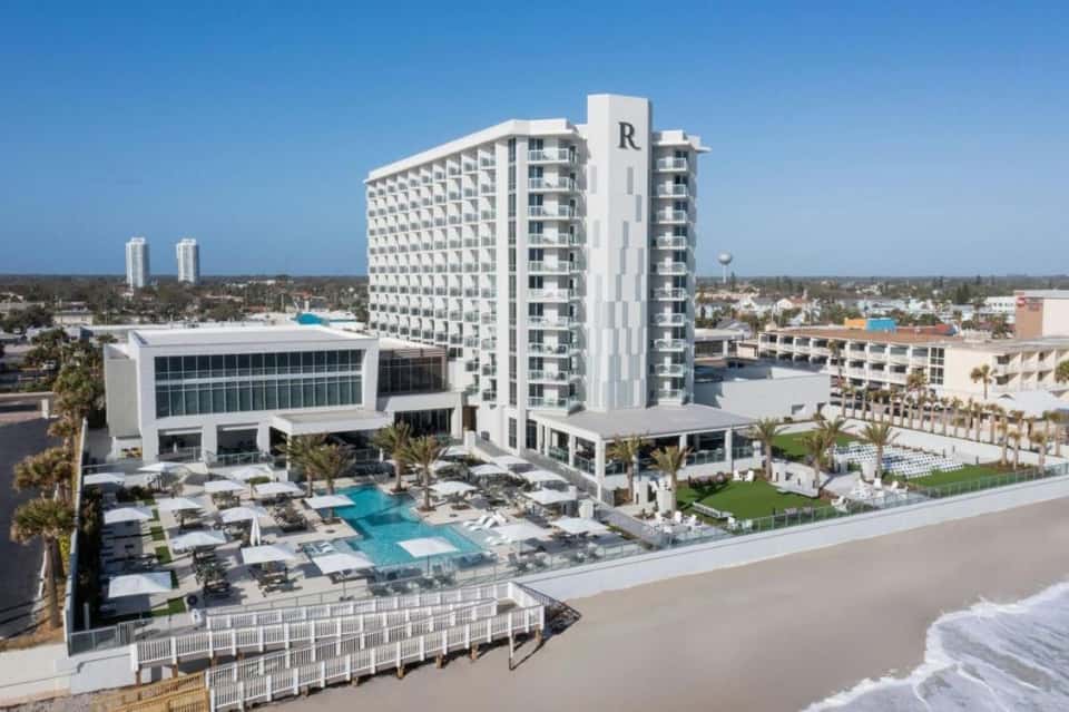 Modern beachfront hotel with white tower, pool area, and direct beach access with white sand