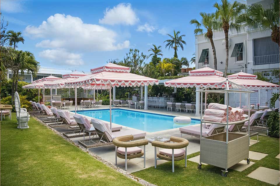Elegant pool area with pink and white striped umbrellas, lounge chairs, and manicured lawn