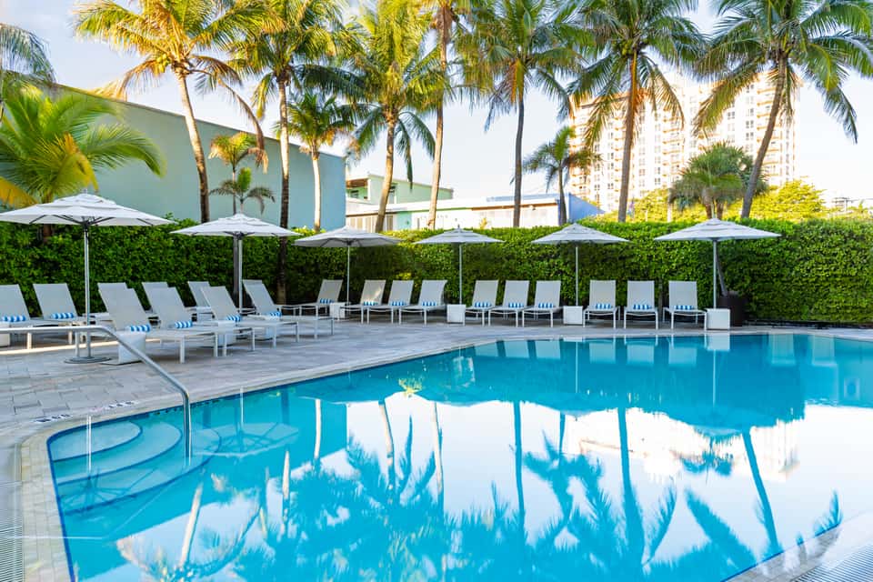 Resort pool deck with lounge chairs, umbrellas, palm trees, and ocean view in tropical setting