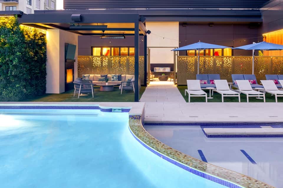 Illuminated resort pool deck at dusk with lounge chairs, fire pit, and covered seating areas