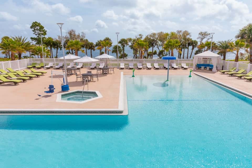Resort pool area with loungers, umbrellas, hot tub, and palm trees surrounding the deck