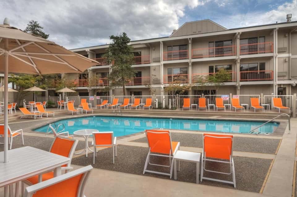 Resort pool with orange lounge chairs, white umbrellas, and multi-story building backdrop