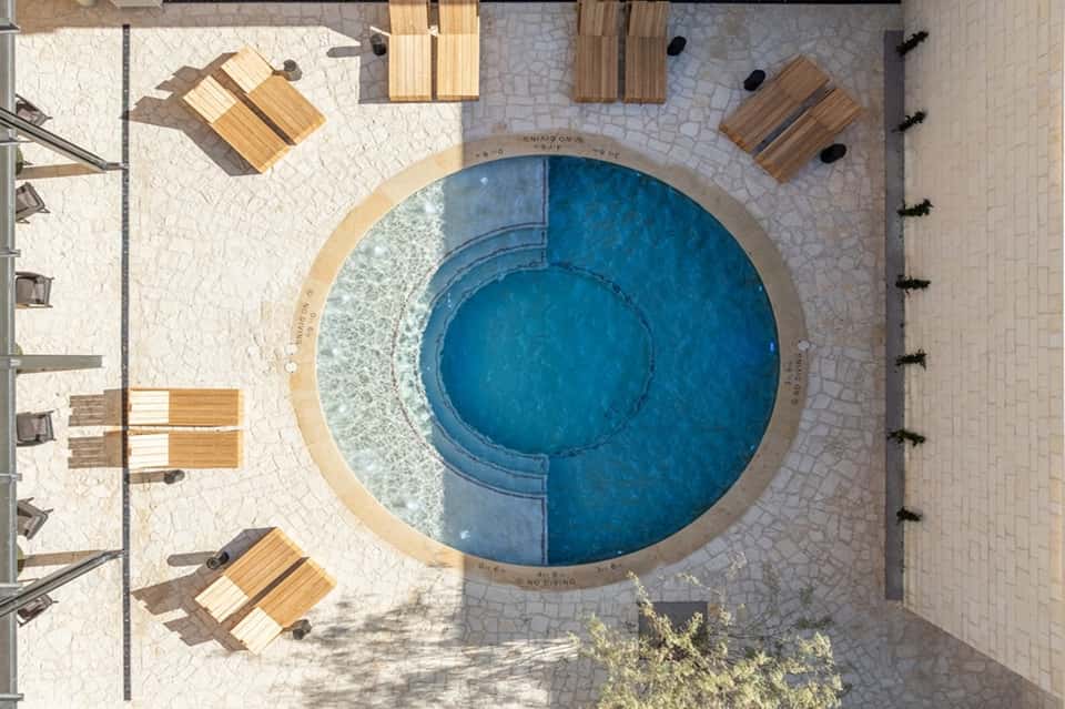Aerial view of circular blue pool surrounded by wooden loungers and patio