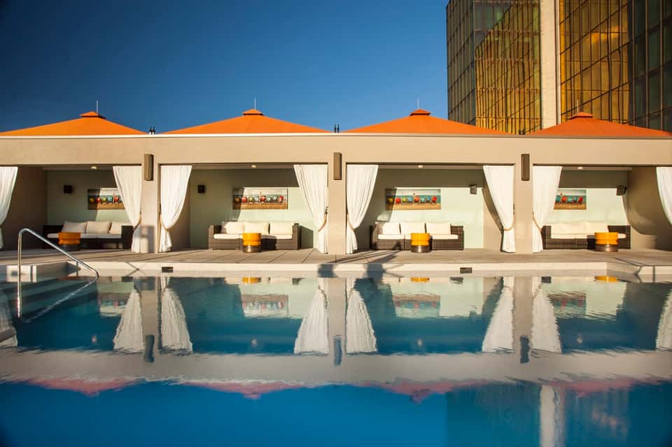 Modern poolside cabanas with orange umbrellas and white curtains