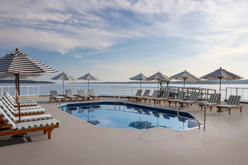 Waterfront pool with striped umbrellas, lounge chairs, and water views at luxury resort