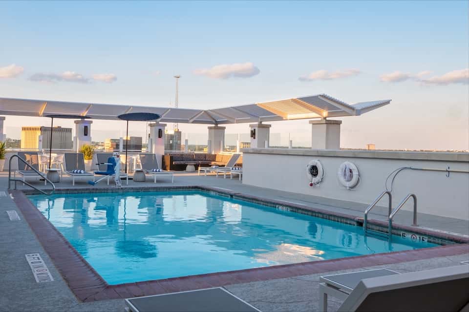Rooftop pool with blue water, modern pergola shade structure, and city skyline views