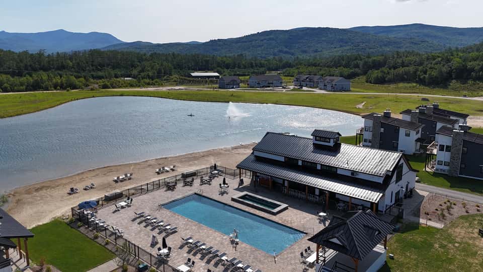 Resort with pool, beach access, and mountain views; modern architecture beside natural lake