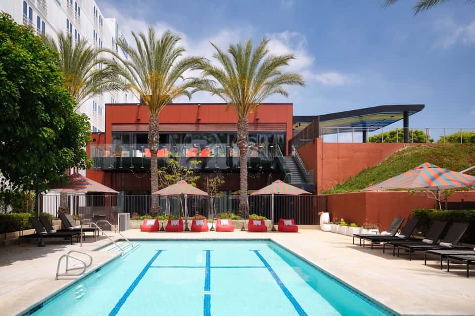 Modern lap pool with red umbrellas and lounge chairs facing contemporary building