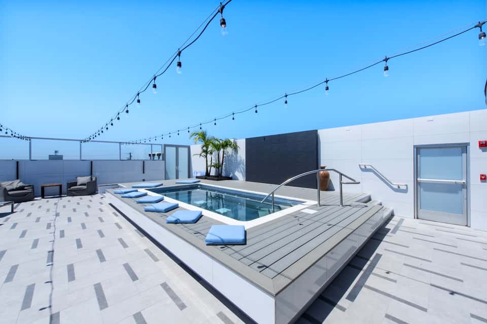 Modern rooftop pool deck with hot tub, blue loungers, string lights, and glass barriers