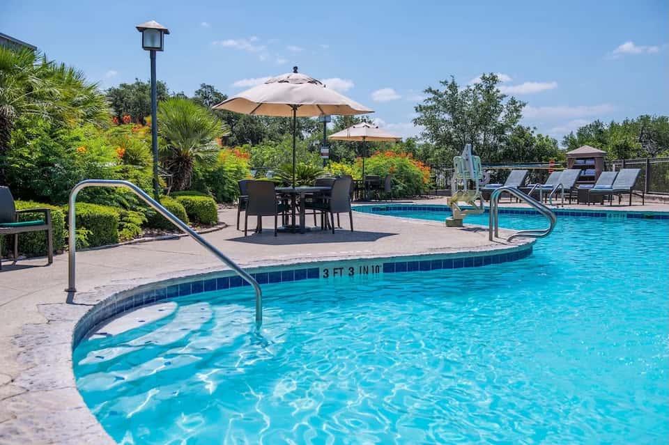Resort pool with curved spa, umbrellas, dining tables, and lush landscaping