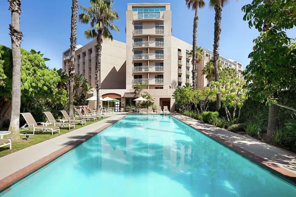 Multi-story hotel with lap pool, palm trees, lounge chairs, and desert landscaping