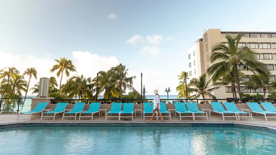 Resort pool with turquoise lounge chairs, palm trees, and ocean view in background