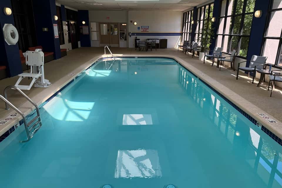 Indoor heated swimming pool with large windows, seating area, and warm natural lighting