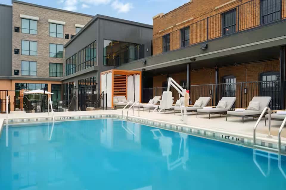 Resort pool surrounded by lounge chairs with modern brick and glass buildings