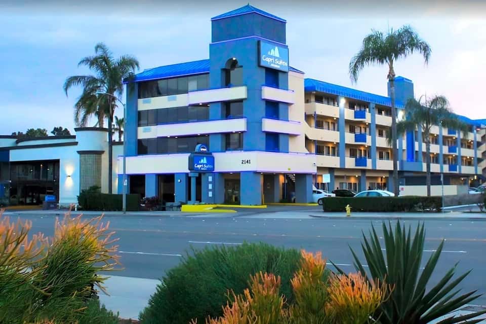 Blue and white mid-rise hotel building with palm trees and landscaping on street corner