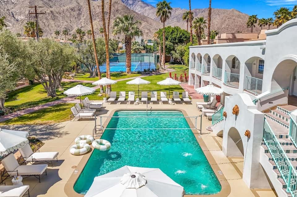 Desert resort courtyard with rectangular pool, white umbrellas, and palm trees