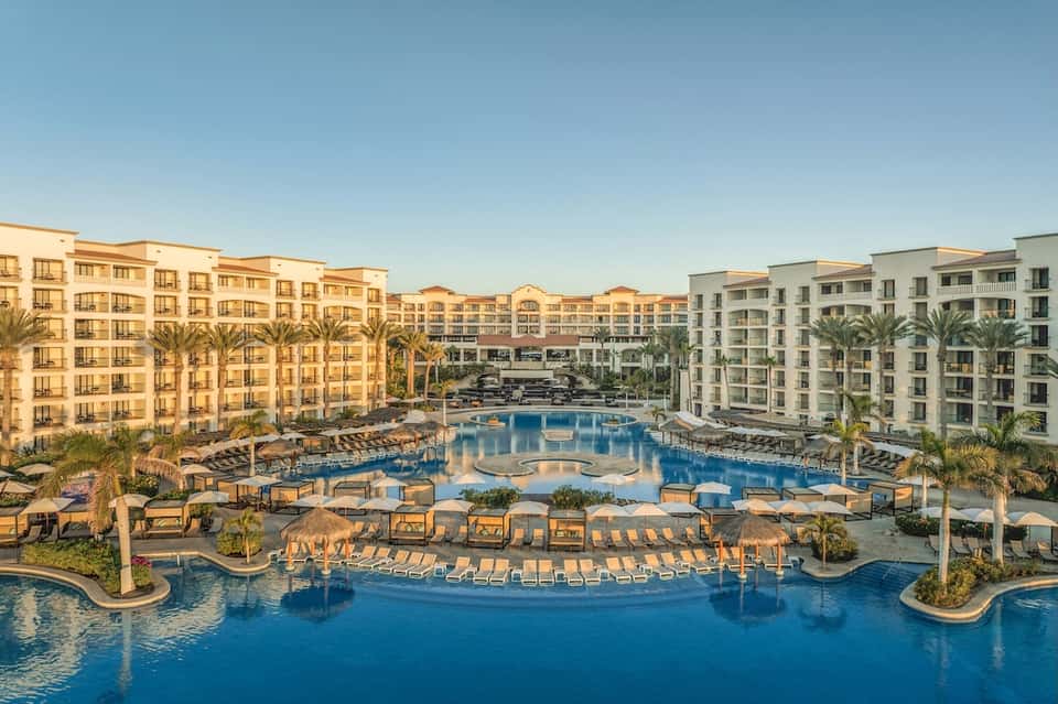 Aerial view of large resort with multiple pools, thatched umbrellas, palm-lined courtyards, and apartment towers